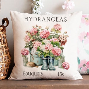 May include: A white pillow with a floral design featuring pink hydrangeas in blue buckets. The pillow has the text "Hydrangeas Bouquets 45c" printed on it.