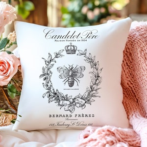 Puede incluir: Almohada blanca con un diseño en blanco y negro que presenta una abeja, una corona y el texto "Candelot Pere Maison Fondée en 1854 Officier d'Académie Les Abeilles Bernard Frères Successeurs 148, Faubourg S. Denis, 148".