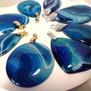 May include: A collection of polished blue agate pendants in various shapes, including oval, teardrop, and heart. Each pendant features unique swirling patterns and is fitted with either gold or silver-colored bails for attaching to a chain.