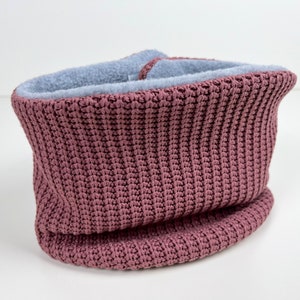 Könnte beinhalten: Ein gestrickter Cowl-Schal in Staubrosa mit einem weichen, hellblauen Fleecefutter. Die Rippenstrickstruktur ist sichtbar und schafft ein warmes und gemütliches Accessoire. Dieser Halswärmer ist für kaltes Wetter konzipiert.