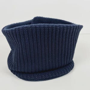 May include: A navy blue knitted neck warmer. The ribbed knit fabric is visible, and the neck warmer is folded over. The item is made of a soft material and is designed to keep the neck warm. The neck warmer is a winter accessory.
