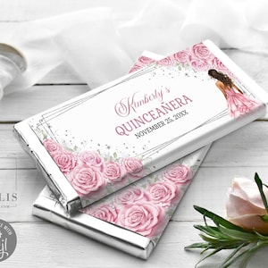 May include: Two rectangular chocolate bar wrappers featuring a white background with pink roses, silver geometric lines, and a graphic of a person in a pink dress. The text reads Kimberly's QUINCEAÑERA NOVEMBER 25, 20XX in pink and black lettering.