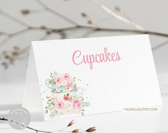 Puede incluir: Una tarjeta blanca plegada con el texto rosa Cupcakes y una ilustración en acuarela de dos tazas de té apiladas llenas de rosas rosas y hojas verdes. La tarjeta incluye el pequeño texto SUSELIS.ETSY.COM en la esquina inferior derecha.