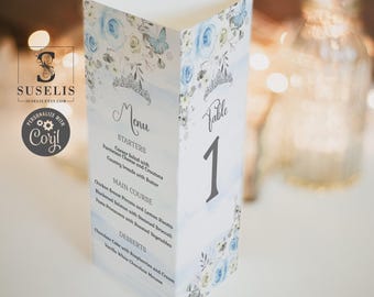 May include: A tall, folded paper menu and table number card featuring a watercolor design of blue roses, butterflies, and a silver tiara. The text includes Menu, Starters, Main Course, Desserts, and Table 1, with listed food items.