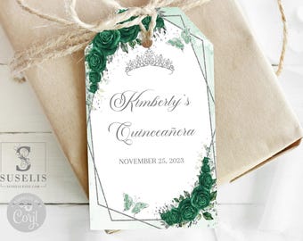 May include: A rectangular gift tag with a white background, featuring dark green roses, a silver tiara illustration, and a geometric silver frame. The text reads Kimberly's Quinceañera and NOVEMBER 25, 2023. Two light green butterflies are visible on the tag.