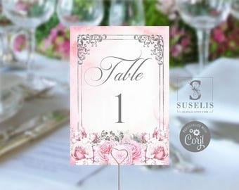May include: A rectangular table number card featuring a soft pink watercolor background, a silver ornate border, and the text Table 1 in a script font. The bottom of the card is decorated with a cluster of detailed pink rose illustrations.