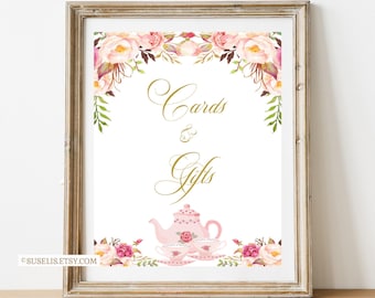 May include: A framed sign featuring the gold text Cards & Gifts in a cursive font. The design includes watercolour illustrations of pink roses and green leaves at the top and bottom, with a pink teapot and two teacups at the bottom centre.