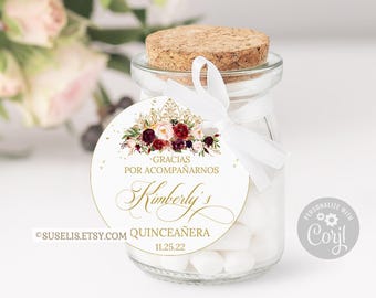 May include: A clear glass jar filled with white candies, topped with a cork stopper and a white ribbon. A round tag features a floral illustration, gold crown, and the text: GRACIAS POR ACOMPAÑARNOS, Kimberly's, QUINCEAÑERA, 11.25.22.