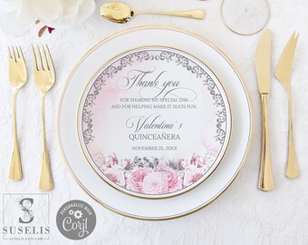 May include: A white dinner plate with a gold rim featuring a pink floral design and text that reads Thank you for sharing my special day and for helping make it such fun. Valentina's Quinceañera November 25, 20XX, with gold cutlery.