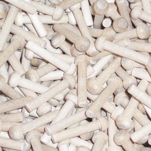 May include: A close-up image of a pile of wooden dowels with rounded tops. The dowels are all the same size and are a light brown color.