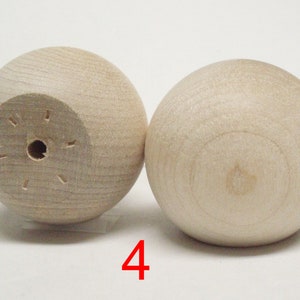 May include: Two wooden balls, one with a hole in the center and the other with a smooth surface. The balls are light brown in color and are sitting on a white surface. The number "4" is written in red below the balls.