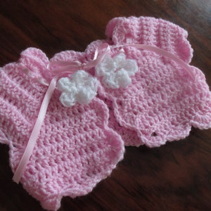 Puede incluir: Dos jers&eacute;is de beb&eacute; de ganchillo rosa con adornos de flores de ganchillo blanco.