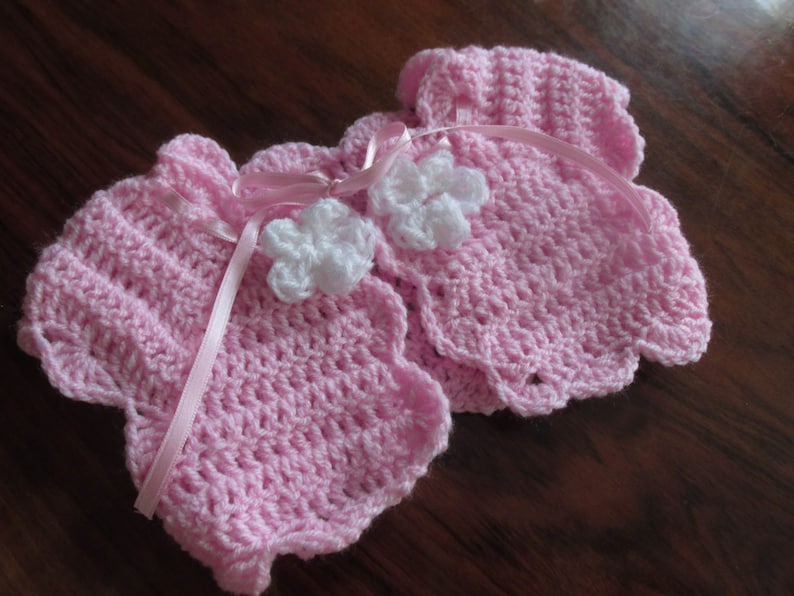 Puede incluir: Dos jers&eacute;is de beb&eacute; de ganchillo rosa con adornos de flores de ganchillo blanco.