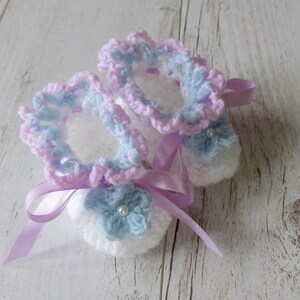May include: A pair of crocheted baby booties in white, pink, and blue with a satin ribbon tied around them.
