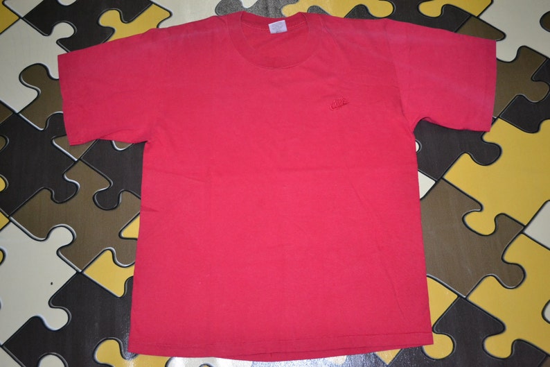 May include: A red short-sleeved t-shirt with a small embroidered logo on the left chest.