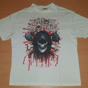 Puede incluir: Camiseta blanca con un gráfico de calavera en blanco y negro. La calavera está rodeada de salpicaduras de sangre y armas cruzadas. El texto "RIGOR MORTIS" está impreso en rojo sobre la calavera.