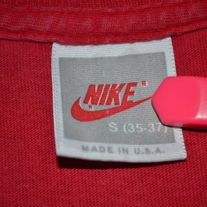 May include: White tag with a red Nike logo and the text "NIKE" in red with a registered trademark symbol. The tag also says "S (35-37)" and "MADE IN U.S.A."