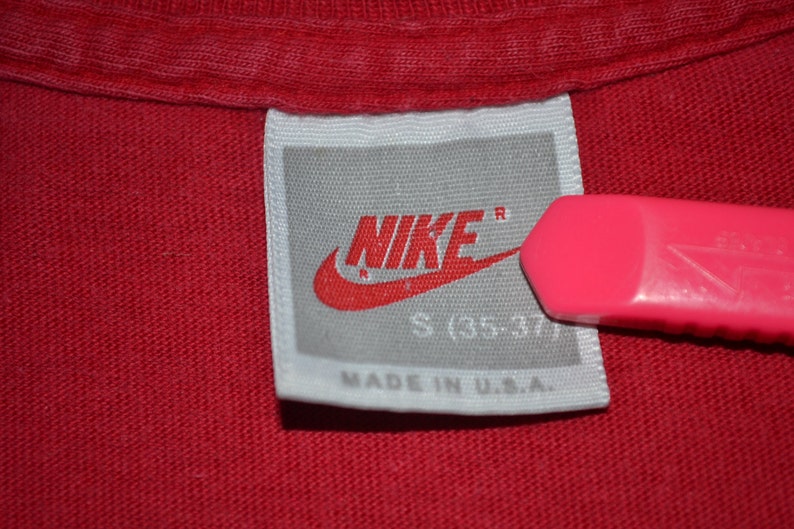 May include: White tag with a red Nike logo and the text "NIKE" in red with a registered trademark symbol. The tag also says "S (35-37)" and "MADE IN U.S.A."