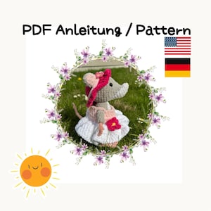 May include: Crochet pattern for a gray mouse wearing a pink dress and hat. The pattern is available in English and German. The image also includes a sun and a floral wreath.