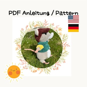 May include: A crochet pattern for a cute gray mouse wearing a green and yellow shirt and a brown hat. The pattern is available in both English and German. The image also includes a sun with a smiley face.