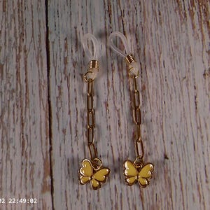 May include: A pair of gold-toned metal chain dangles featuring yellow enamel butterfly charms at the base. Each piece includes a clear silicone loop at the top, secured with a small gold-toned coil, designed for non-pierced attachment.