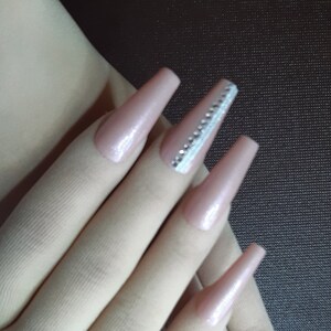 May include: A set of long, nude-colored acrylic nails with a sparkly silver accent on one nail.