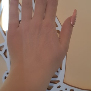 May include: A hand with long, light pink, almond-shaped nails with rhinestones on the ring finger.