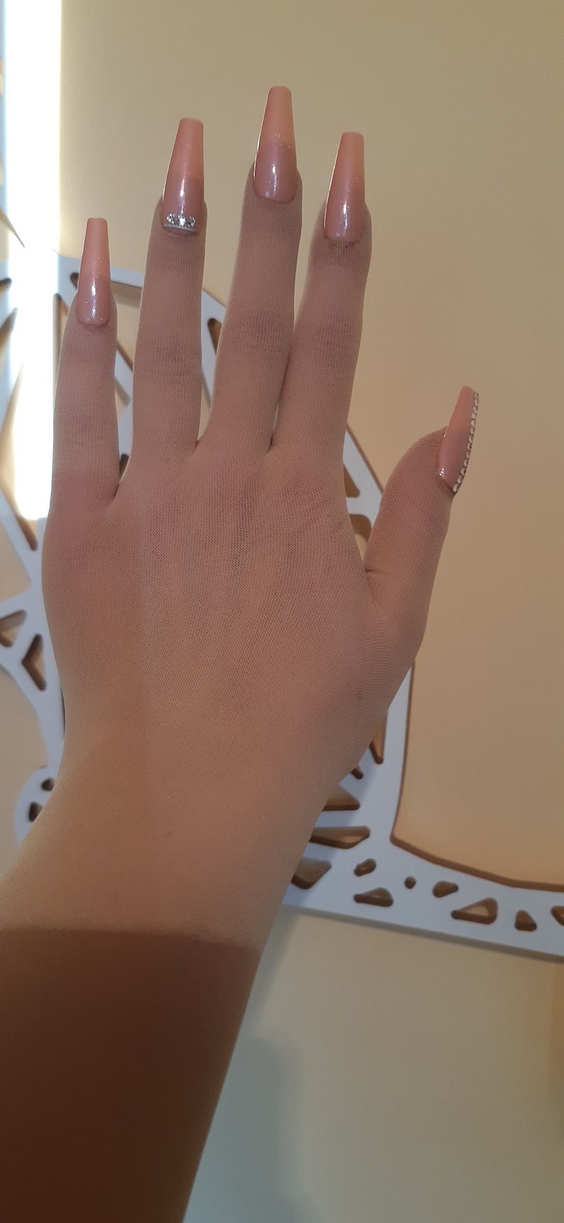 May include: A hand with long, light pink, almond-shaped nails with rhinestones on the ring finger.