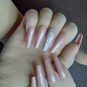 May include: Long, nude-colored, coffin-shaped acrylic nails with a silver glitter accent on one nail. The nails have a subtle shimmer finish.