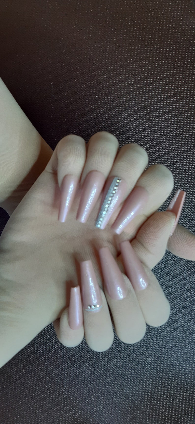 May include: Long, nude-colored, coffin-shaped acrylic nails with a silver glitter accent on one nail. The nails have a subtle shimmer finish.