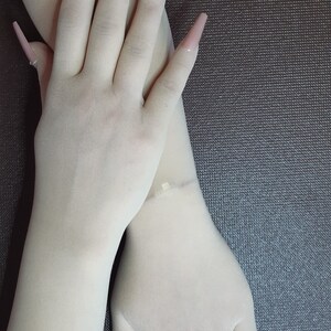 May include: A pair of white long fingerless gloves with nude-colored long acrylic nails. Some of the nails have rhinestones.