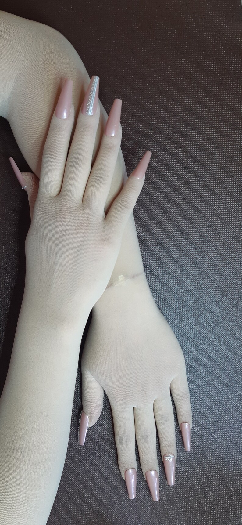May include: A pair of white long fingerless gloves with nude-colored long acrylic nails. Some of the nails have rhinestones.