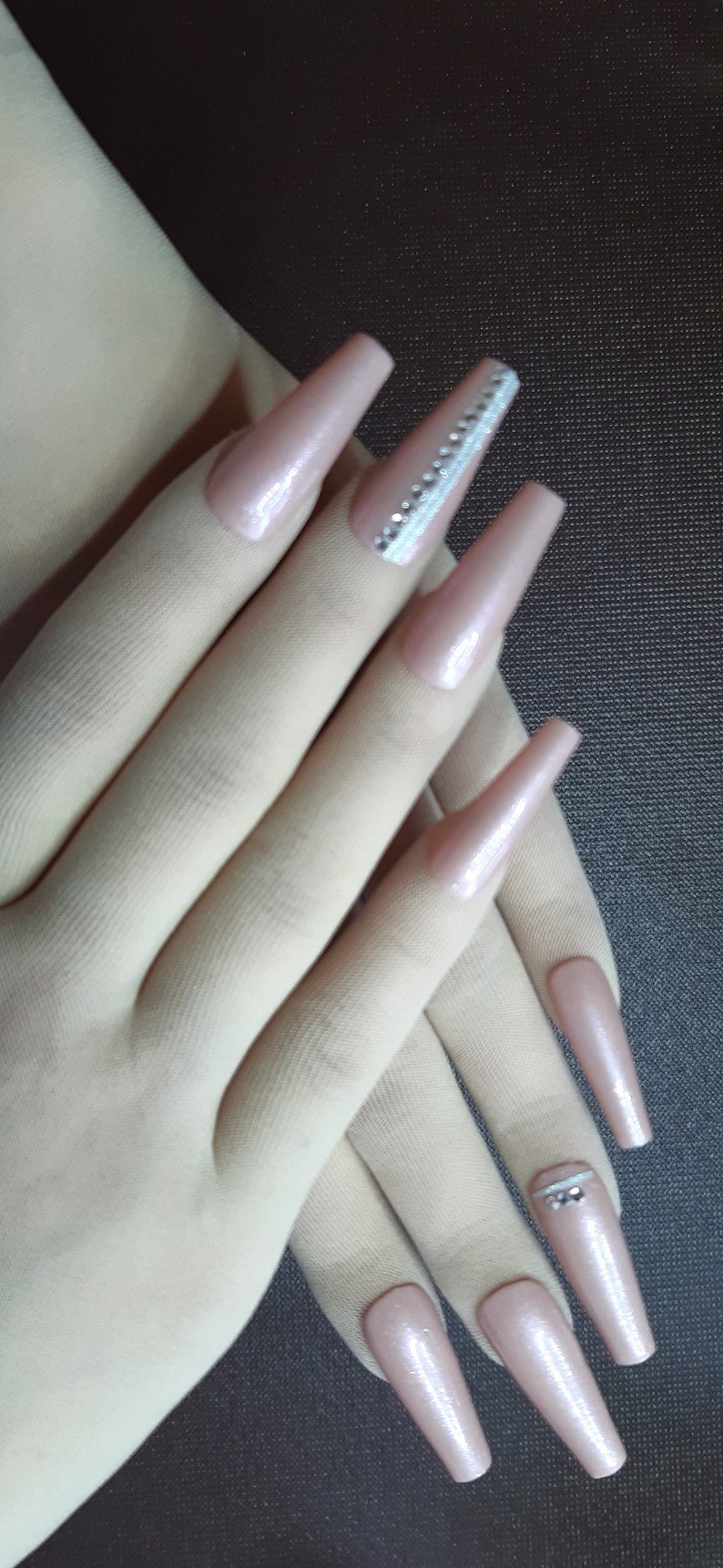 May include: A set of long, nude-colored acrylic nails with a sparkly silver accent on one nail.