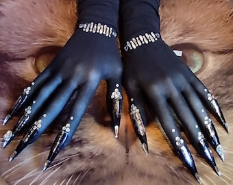 May include: A pair of black gloves with long, pointed black fingernails adorned with silver rhinestones. The gloves are made of a sheer, stretchy material.