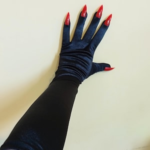 Puede incluir: Un par de guantes largos de satén negro con uñas puntiagudas rojas.