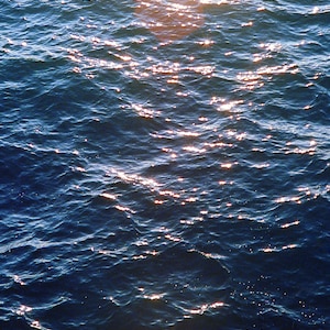 May include: A close-up of the surface of the ocean water with sunlight reflecting off the waves. The water is a deep blue color with white highlights from the sun.