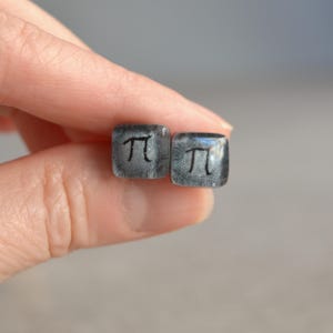 May include: A pair of silver square earrings with a black pi symbol on each earring.