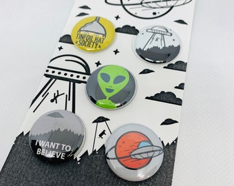 Peut inclure: Un ensemble de six badges ronds avec des motifs d'extraterrestres et d'OVNI. Les badges présentent des illustrations d'un extraterrestre vert, d'un OVNI au-dessus d'une chaîne de montagnes, d'un OVNI au-dessus d'une planète, et le texte "I WANT TO BELIEVE" et "TINFOIL HAT SOCIETY".