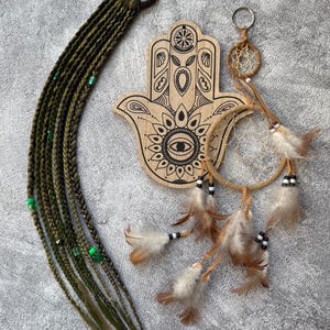 May include: An assortment of bohemian-style accessories. Includes a set of olive green braided hair extensions with green beads, a wooden Hamsa hand with etched details, and a small dreamcatcher keychain with feathers.