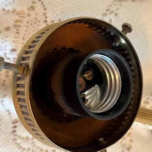 May include: Close-up of a vintage brass light fixture socket. The socket is black and silver, surrounded by a brass housing with screw details. The fixture is designed to hold a light bulb.
