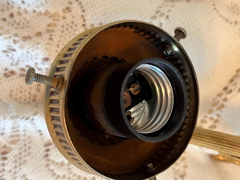 May include: Close-up of a vintage brass light fixture socket. The socket is black and silver, surrounded by a brass housing with screw details. The fixture is designed to hold a light bulb.