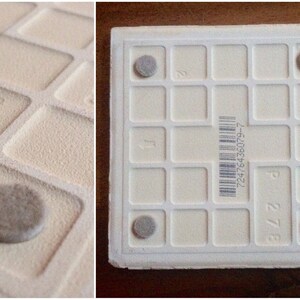 K&ouml;nnte beinhalten: Wei&szlig;e Keramikfliese mit einem Gittermuster und vier grauen Gummif&uuml;&szlig;en auf der Unterseite. Die Fliese hat einen Barcode und die Zahlen "27/8" und "108" sind darauf gedruckt.