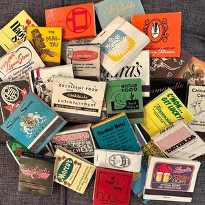 May include: A collection of vintage matchbook covers with various designs and text. The matchbooks feature a variety of themes, including hotels, restaurants, bars, and businesses. Some of the matchbooks have colorful illustrations, while others have simple text designs. The matchbooks are a great example of vintage advertising and ephemera.
