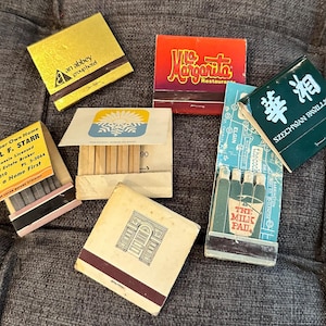 May include: A collection of vintage matchbooks with various designs. The matchbooks include a green matchbook with the text "Szechwan Pavilion", a blue matchbook with the text "The Milk Pad", a yellow matchbook with the text "an abbey group hotel", a red matchbook with the text "Mc Margarita Restaurant", a yellow matchbook with the text "Own Your Own Home Virgil F. Starr Wisconsin Licensed Real Estate Broker PI. 3-5010 PI. 3-3044 Buy a Home First", and a blue and white matchbook with the number "90" printed on it.