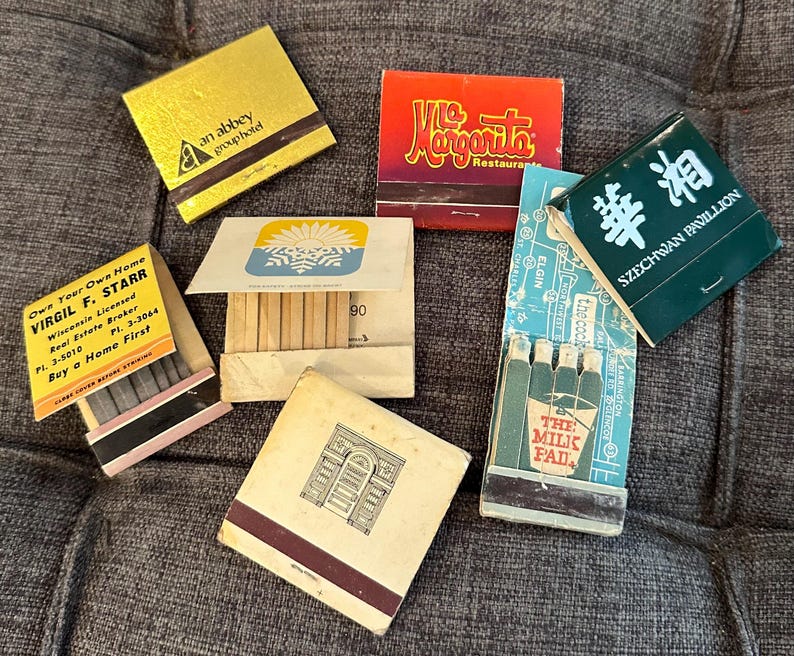 May include: A collection of vintage matchbooks with various designs. The matchbooks include a green matchbook with the text "Szechwan Pavilion", a blue matchbook with the text "The Milk Pad", a yellow matchbook with the text "an abbey group hotel", a red matchbook with the text "Mc Margarita Restaurant", a yellow matchbook with the text "Own Your Own Home Virgil F. Starr Wisconsin Licensed Real Estate Broker PI. 3-5010 PI. 3-3044 Buy a Home First", and a blue and white matchbook with the number "90" printed on it.