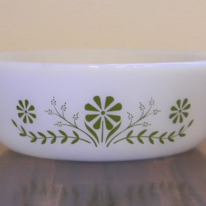 May include: White oval Pyrex baking dish with green floral design. The dish has two handles and a decorative pattern of stylized flowers and leaves. A classic kitchenware item.
