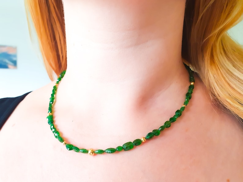 Pu&ograve; includere: Una collana di pietre preziose verdi con perline dorate. La collana &egrave; composta da piccole pietre verdi di forma ovale e perline dorate.