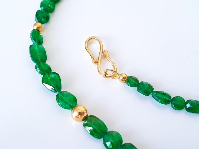 Pu&ograve; includere: Una collana di pietre preziose verdi con perline dorate e una chiusura dorata. La collana &egrave; realizzata con pietre preziose verdi di forma ovale.