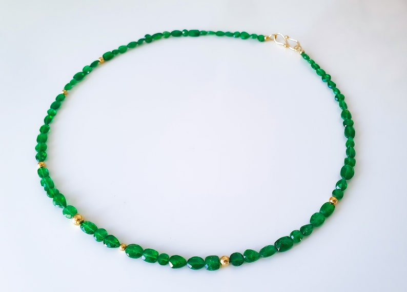 Pu&ograve; includere: Una collana di pietre preziose verdi con perline dorate. La collana &egrave; realizzata con pietre verdi di forma ovale e piccole perline dorate.