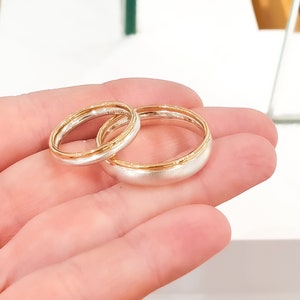May include: Two wedding bands, one with a gold band and the other with a silver band.